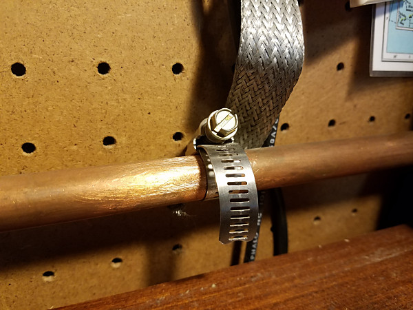 One of the ground connections at the operating position. The braid strap goes to the ground terminal on my 1:1 unun. The other end of the copper pipe ground bus uses hose clamps and a short piece of braid to connect to the cold water pipe coming into the house.